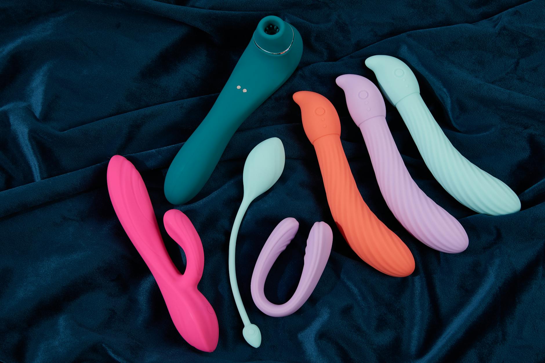 Close-up of hand holding an orange vibrator on a minimalist purple background