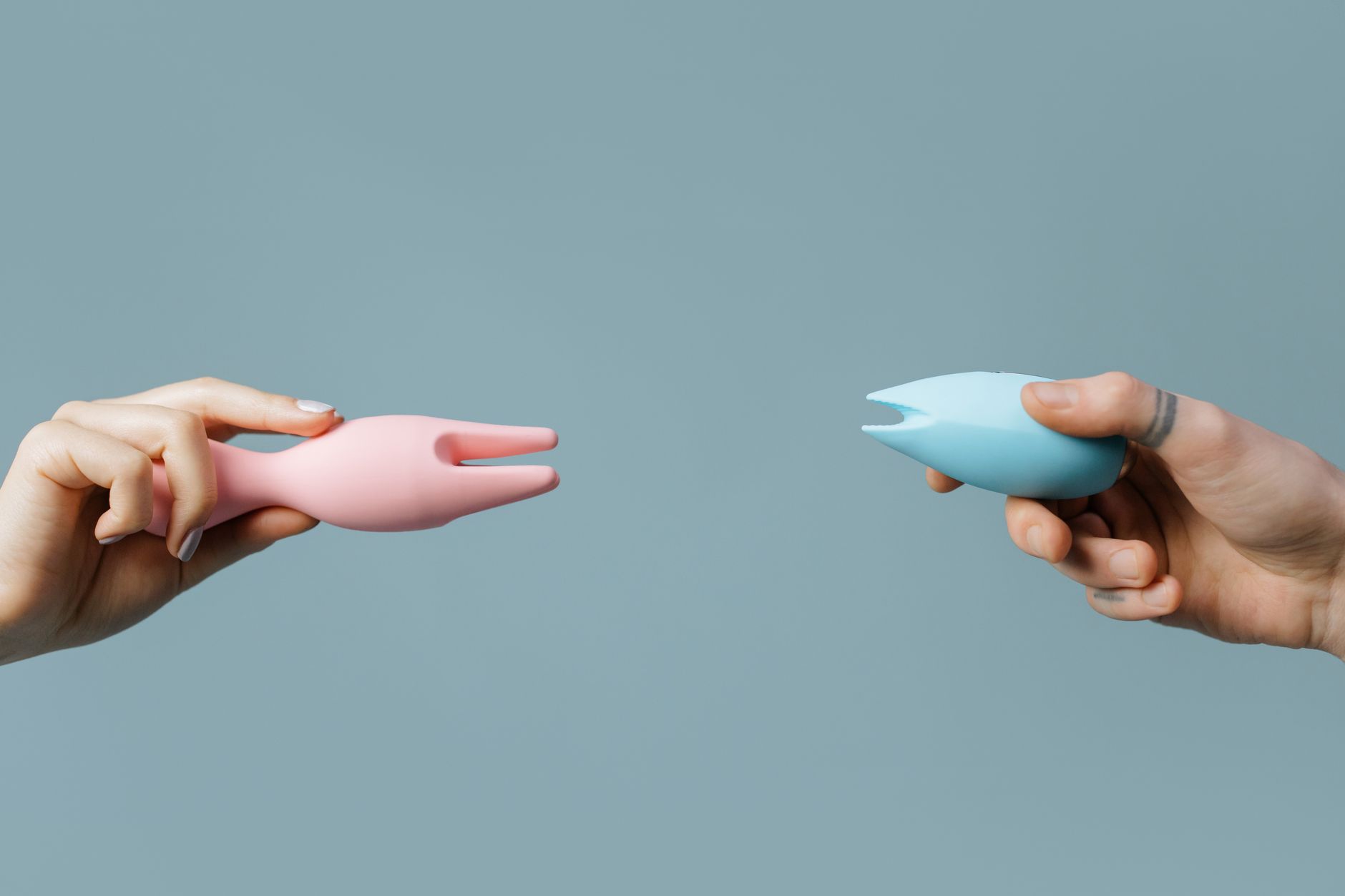 Close-up of hands holding a blue clitoral vibrator against a knitted sweater