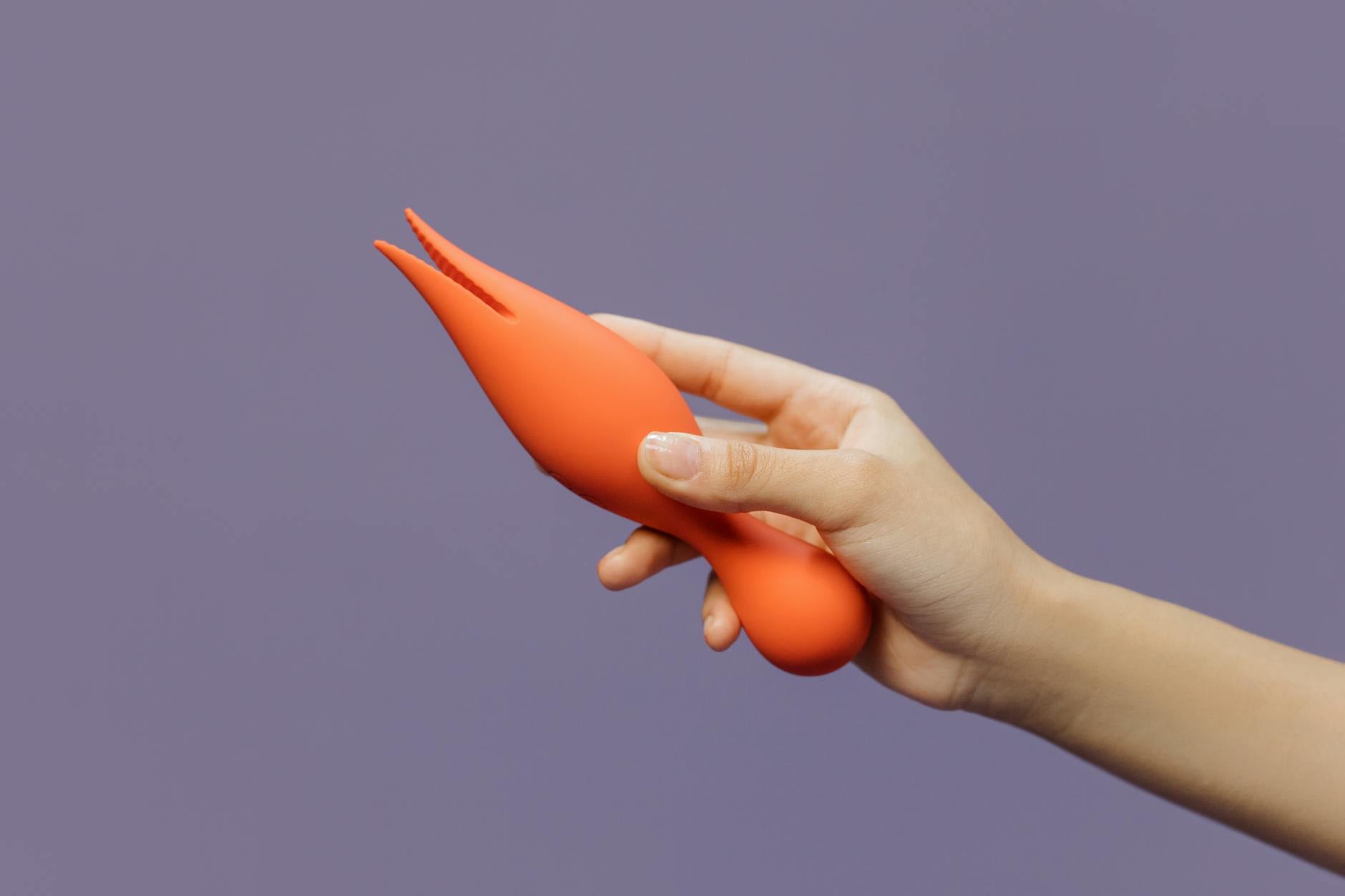 Close-up of a hand holding a lemon vibrator against a minimalistic purple backdrop