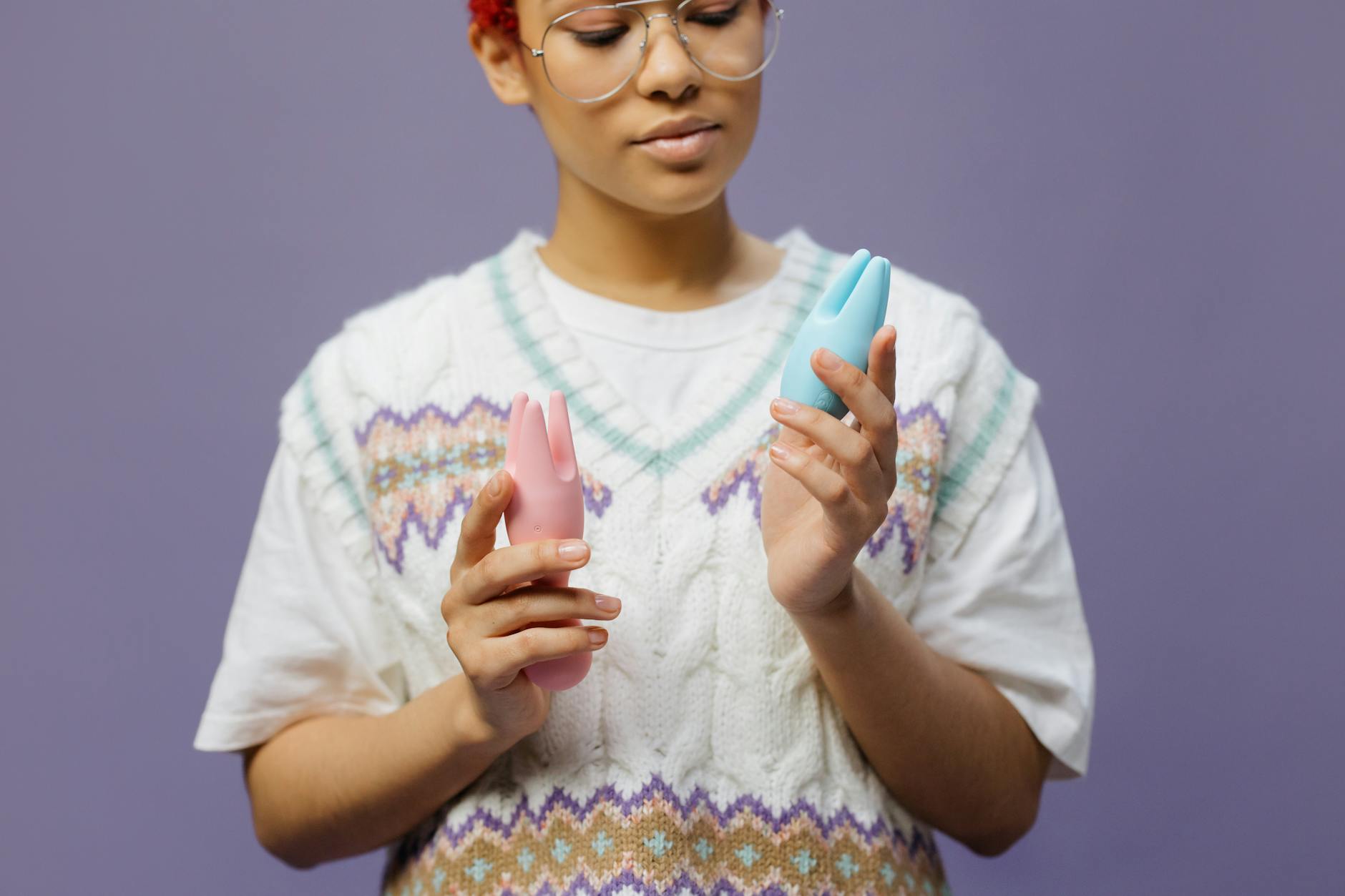Woman in glasses holding colorful silicone vibrators thoughtfully