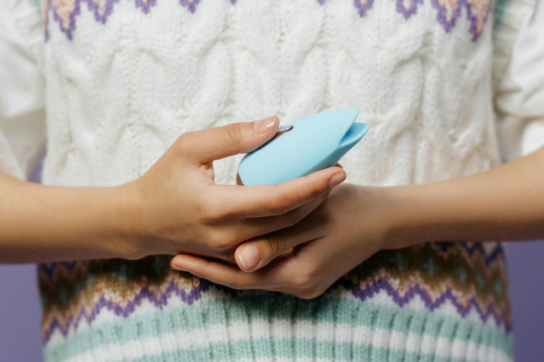 Close-up of hands holding a personal massager against a knitted sweater, representing intimate self-care during anxious moments.